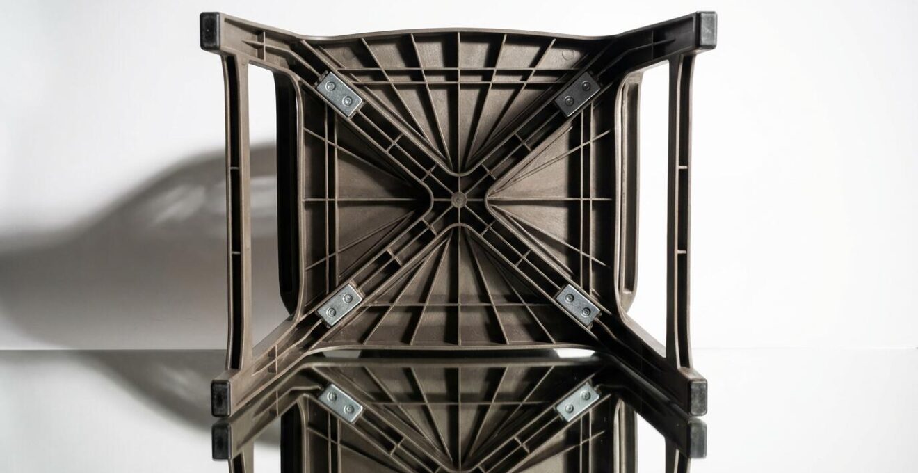Vista dal basso di una sedia da giardino mostrando nervature di rinforzo, supporti a croce e inserti metallici strutturali
