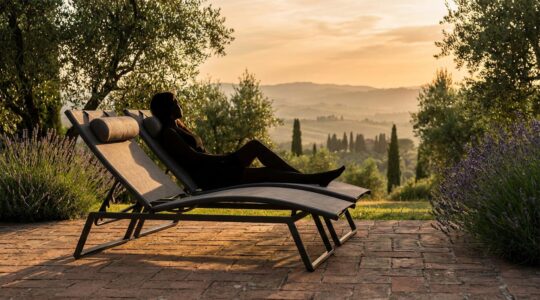 Vista ravvicinata di una sedia da giardino ergonomica in alluminio e textilene con cuscino lombare, posizionata in un giardino mediterraneo italiano